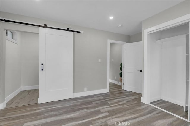 unfurnished bedroom featuring a barn door and light hardwood / wood-style flooring