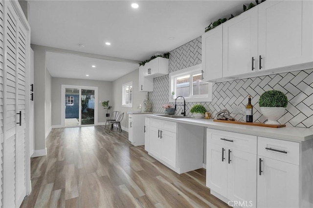 kitchen with sink, backsplash, light hardwood / wood-style floors, and white cabinets