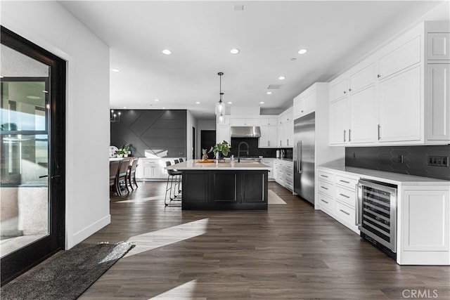 kitchen featuring built in fridge, decorative light fixtures, white cabinets, beverage cooler, and a kitchen island with sink