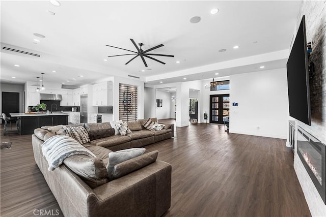 living room with sink, dark wood-type flooring, a large fireplace, and french doors