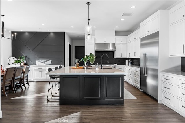 kitchen featuring white cabinetry, decorative light fixtures, an island with sink, and built in refrigerator