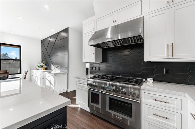 kitchen with dark wood-type flooring, light stone countertops, white cabinets, decorative backsplash, and range with two ovens