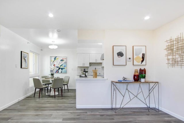 kitchen with white cabinetry, kitchen peninsula, hardwood / wood-style floors, and decorative backsplash