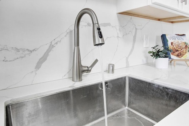 room details featuring sink, decorative backsplash, and white cabinets