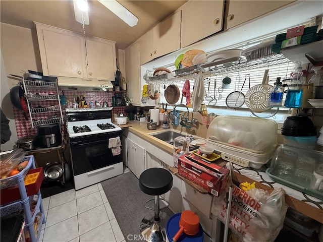 kitchen featuring white cabinets, sink, light tile patterned floors, and range with gas stovetop