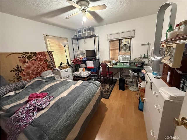 bedroom with cooling unit, ceiling fan, a textured ceiling, and light wood-type flooring