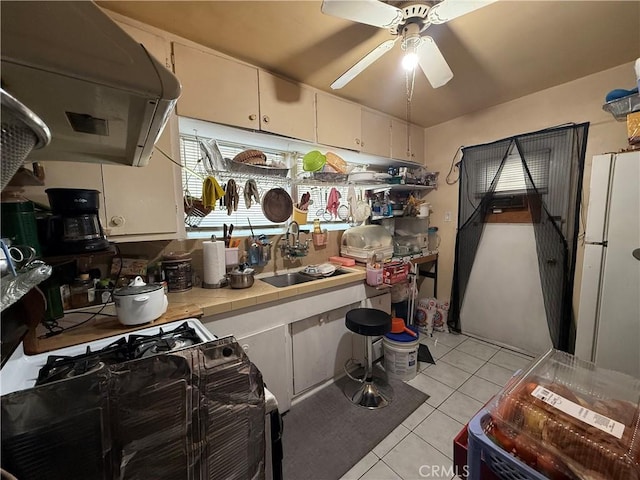 kitchen with gas stove, sink, tile countertops, light tile patterned floors, and exhaust hood