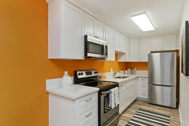 kitchen with stainless steel appliances, white cabinetry, sink, and hardwood / wood-style floors