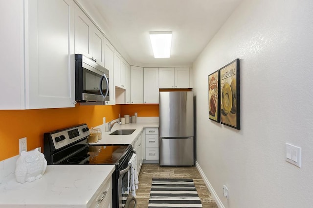 kitchen with sink, dark wood-type flooring, appliances with stainless steel finishes, white cabinetry, and light stone countertops