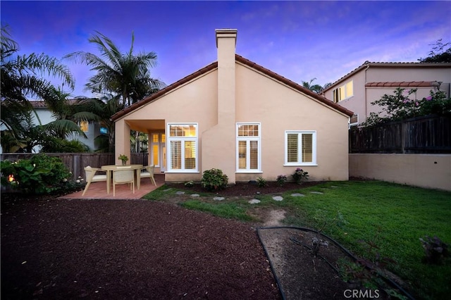 back house at dusk featuring a patio area and a lawn