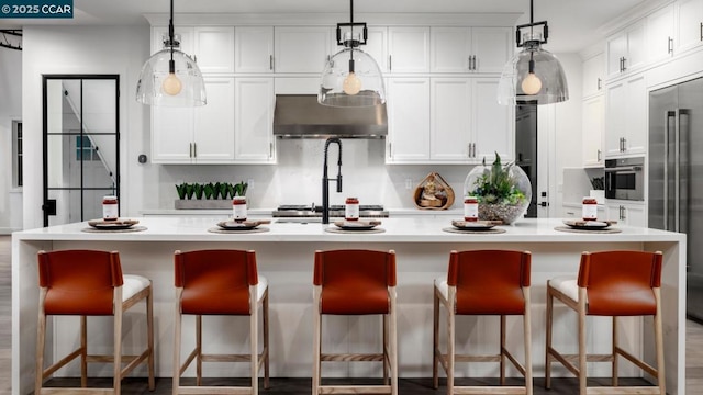 kitchen featuring stainless steel appliances, decorative light fixtures, a breakfast bar, and an island with sink