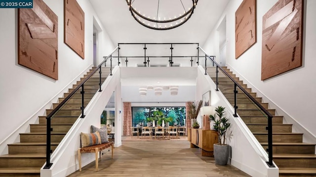 stairway featuring an inviting chandelier, wood-type flooring, and a high ceiling