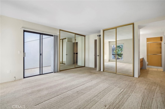 unfurnished bedroom with multiple closets, light colored carpet, and ensuite bath