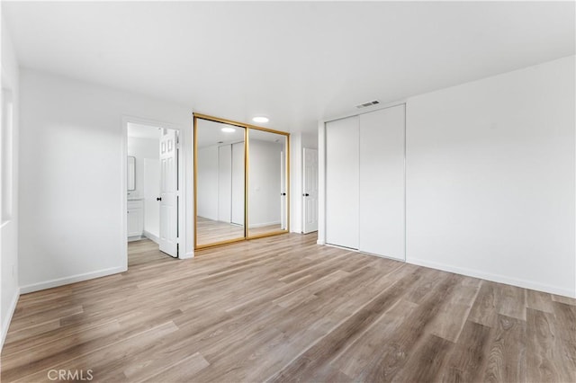 unfurnished bedroom with ensuite bath, light hardwood / wood-style flooring, and two closets