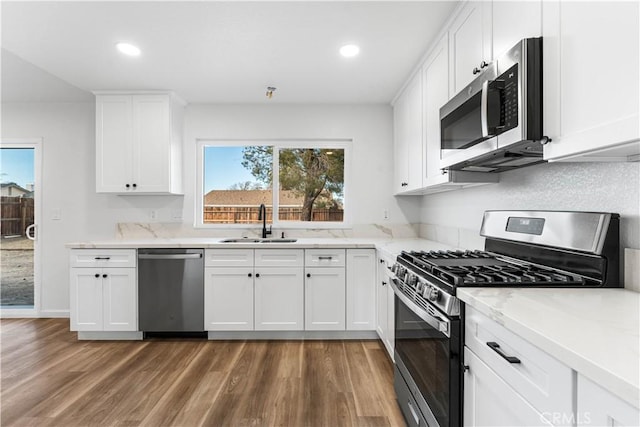 kitchen with sink, dark wood-type flooring, appliances with stainless steel finishes, white cabinetry, and light stone countertops