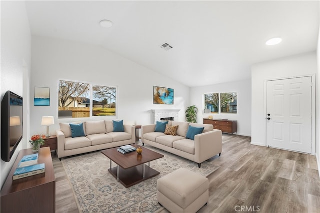 living room with lofted ceiling, a brick fireplace, and light hardwood / wood-style floors