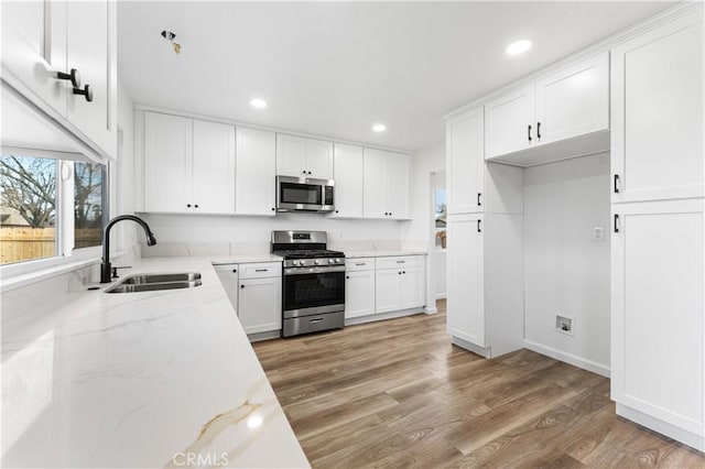 kitchen featuring sink, light stone counters, wood-type flooring, stainless steel appliances, and white cabinets