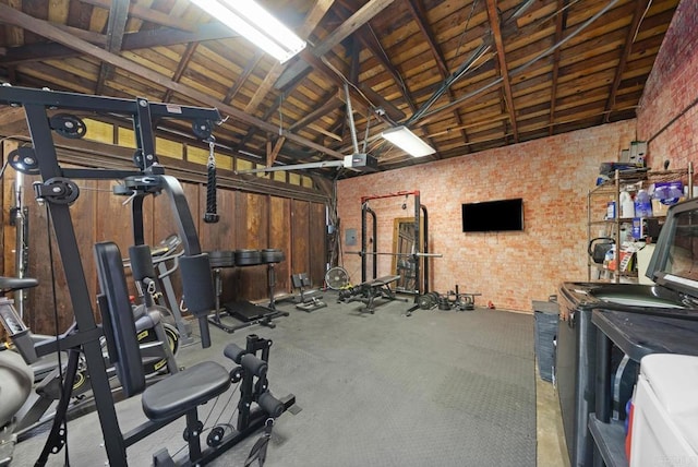 exercise room with a garage, high vaulted ceiling, and brick wall