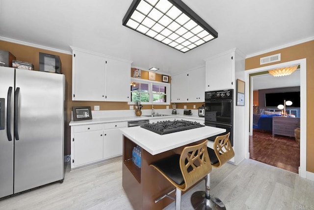 kitchen featuring visible vents, a kitchen island, a breakfast bar area, light countertops, and black appliances