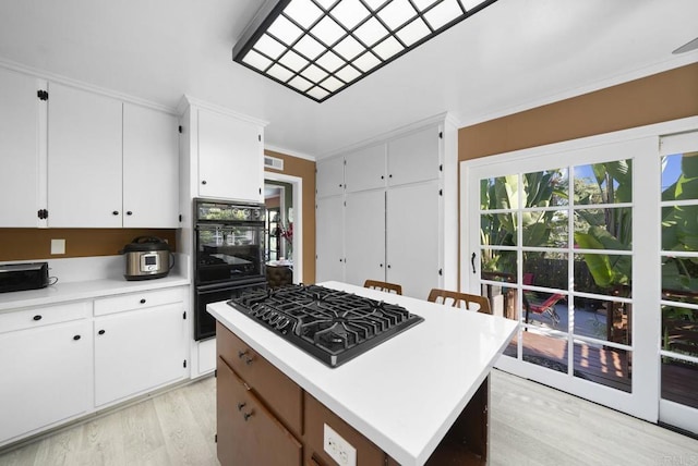 kitchen with light countertops, ornamental molding, white cabinetry, light wood-type flooring, and black appliances