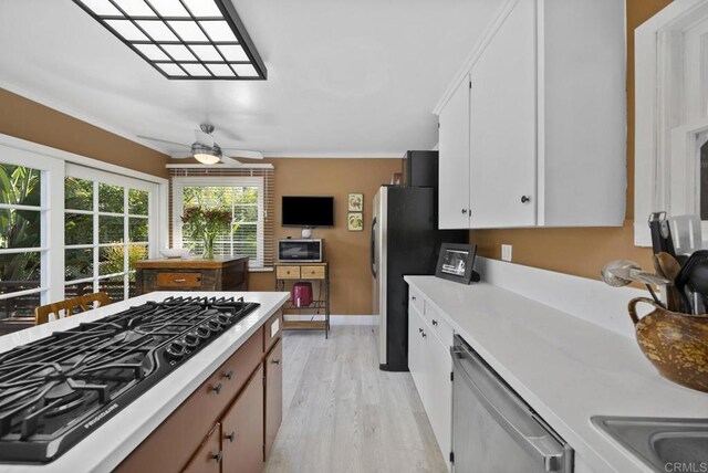 kitchen with light wood-style flooring, white cabinets, light countertops, ornamental molding, and appliances with stainless steel finishes