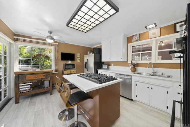 kitchen with a kitchen island, a sink, white cabinets, light countertops, and appliances with stainless steel finishes