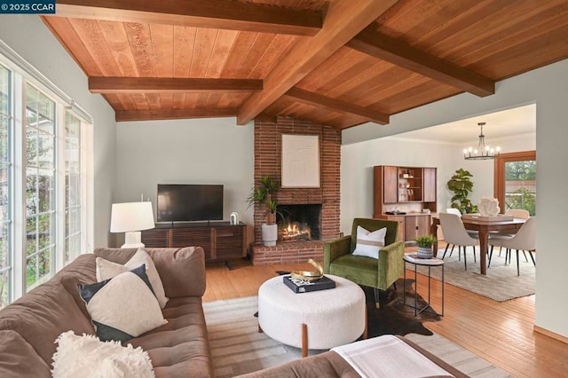 living room with an inviting chandelier, lofted ceiling with beams, a brick fireplace, wooden ceiling, and light wood-type flooring