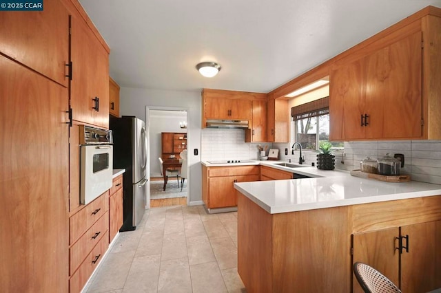 kitchen featuring tasteful backsplash, sink, oven, stainless steel fridge, and kitchen peninsula