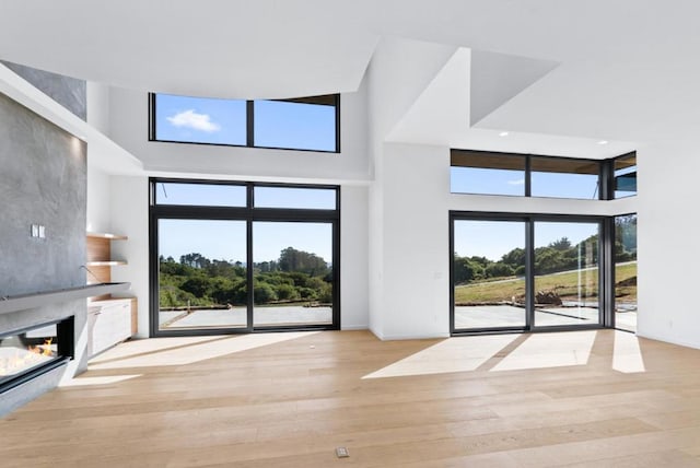 unfurnished living room featuring a towering ceiling, plenty of natural light, and light hardwood / wood-style floors