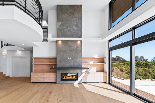 unfurnished living room featuring a towering ceiling, a fireplace, and light wood-type flooring