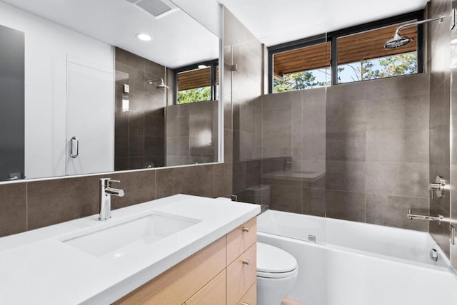 full bathroom featuring combined bath / shower with glass door, tile walls, backsplash, vanity, and toilet