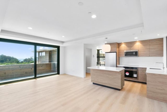 kitchen featuring sink, decorative light fixtures, a raised ceiling, a kitchen island, and stainless steel appliances