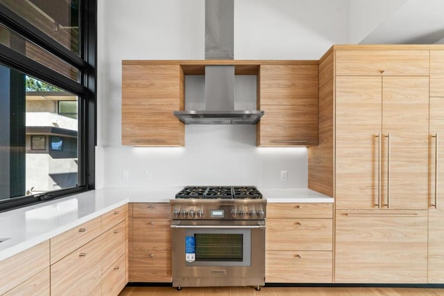 kitchen with high end stainless steel range oven, light brown cabinets, and wall chimney range hood