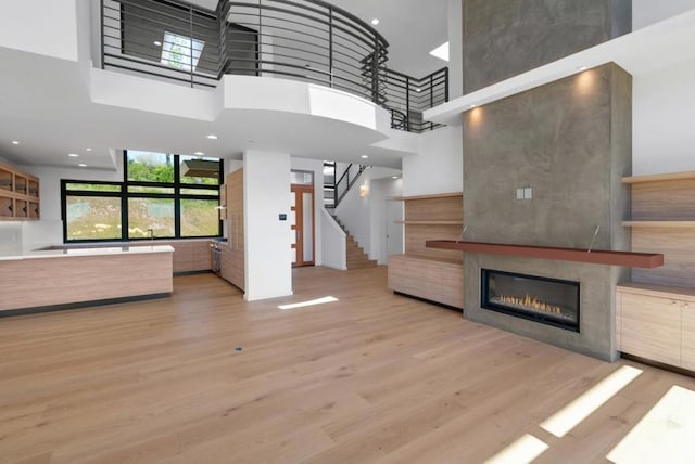 unfurnished living room with light hardwood / wood-style floors, a tile fireplace, and a high ceiling