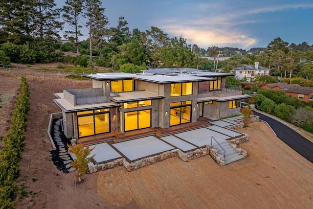 back house at dusk featuring a patio and a balcony