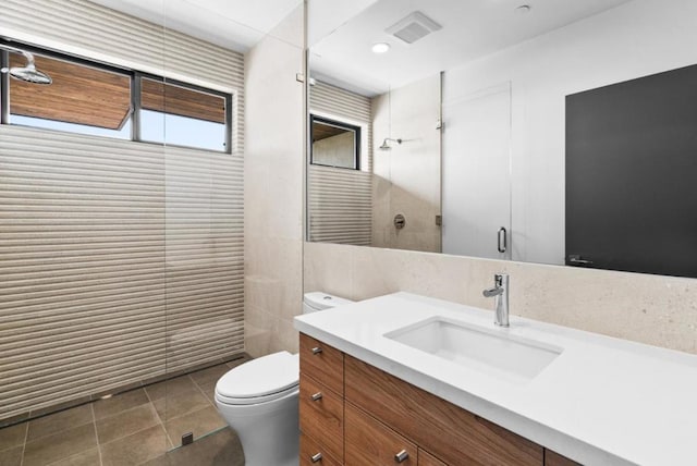 bathroom featuring toilet, tile walls, vanity, a shower with door, and tile patterned flooring