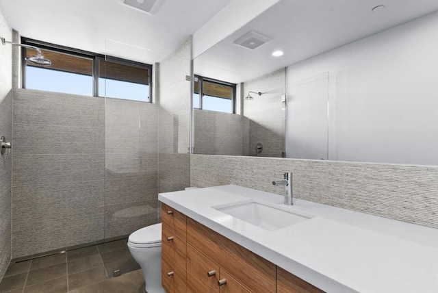 bathroom featuring a tile shower, tile walls, vanity, toilet, and tile patterned floors