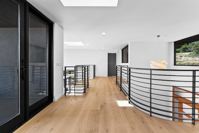 hall with light hardwood / wood-style flooring, a wall of windows, and a skylight