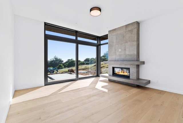 unfurnished living room with floor to ceiling windows, a tiled fireplace, and light wood-type flooring