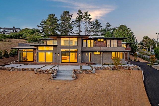 back house at dusk featuring a balcony and a patio area