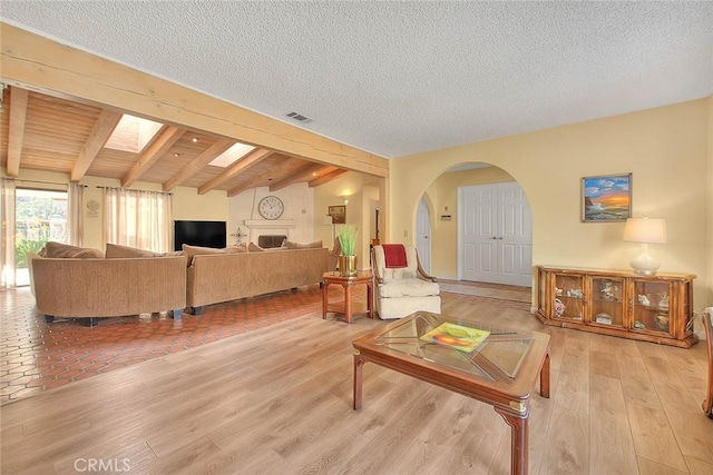 living room featuring lofted ceiling with skylight, light hardwood / wood-style flooring, and a textured ceiling