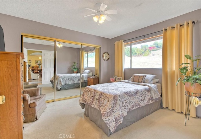 bedroom with ceiling fan, light colored carpet, a closet, and a textured ceiling