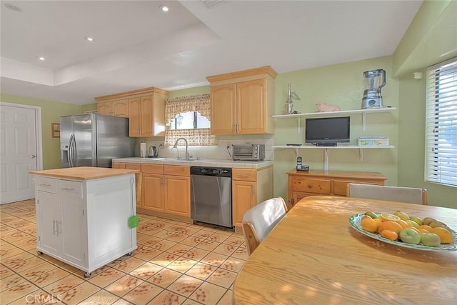 kitchen featuring appliances with stainless steel finishes, sink, a center island, a tray ceiling, and light brown cabinets