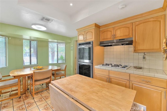 kitchen featuring light brown cabinetry, tasteful backsplash, tile countertops, white gas stovetop, and stainless steel double oven