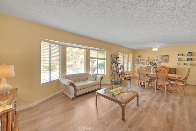 living room featuring ceiling fan, light hardwood / wood-style floors, and a textured ceiling