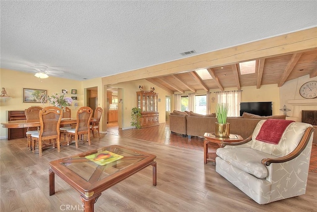 living room featuring vaulted ceiling with skylight, a textured ceiling, and light hardwood / wood-style flooring