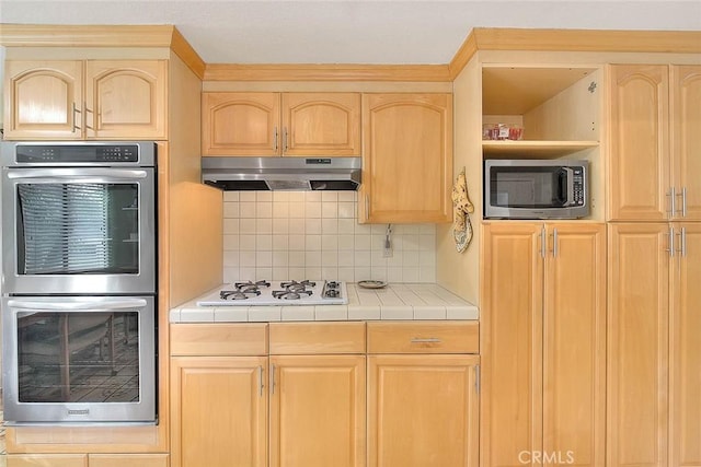 kitchen featuring stainless steel appliances, tile counters, decorative backsplash, and light brown cabinets