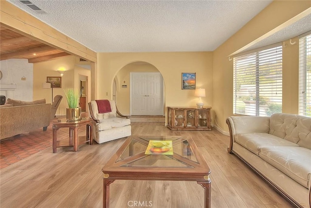 living room with light hardwood / wood-style flooring, beamed ceiling, and a textured ceiling