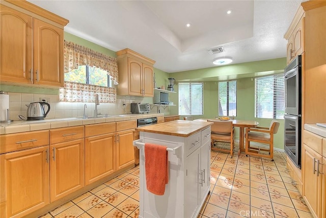 kitchen featuring sink, tile countertops, a kitchen island, a healthy amount of sunlight, and backsplash