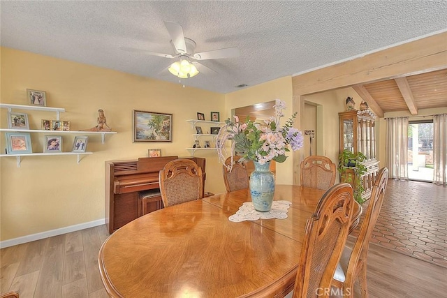 dining room with vaulted ceiling with beams, ceiling fan, a textured ceiling, and light wood-type flooring